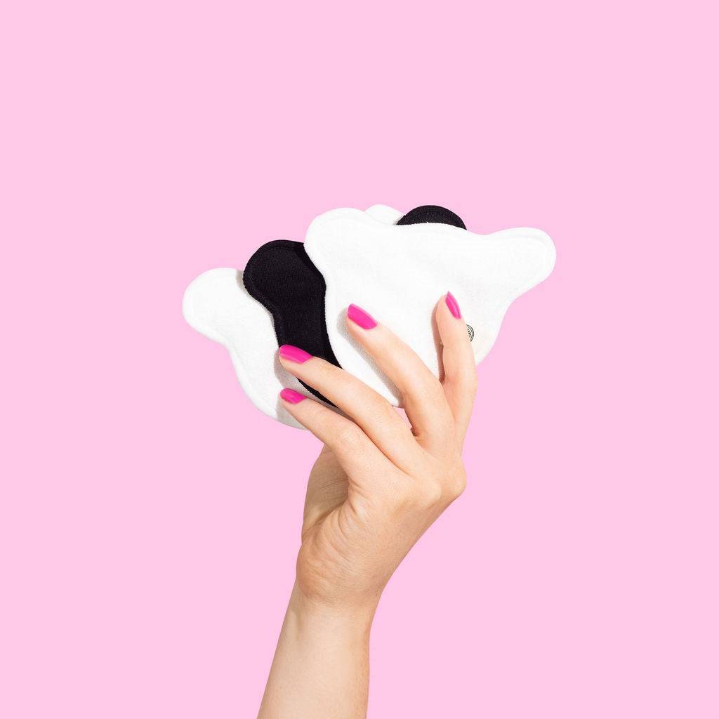 Hand holding reusable black and white cotton pads against pink background